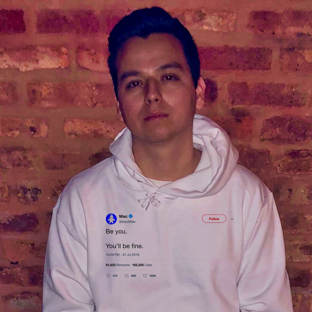 Hiram from the Chi sitting down against a brick wall, wearing a Tee Tweets hoodie that says, 'Be you. You'll be fine,' a tweet from Mac Miller.