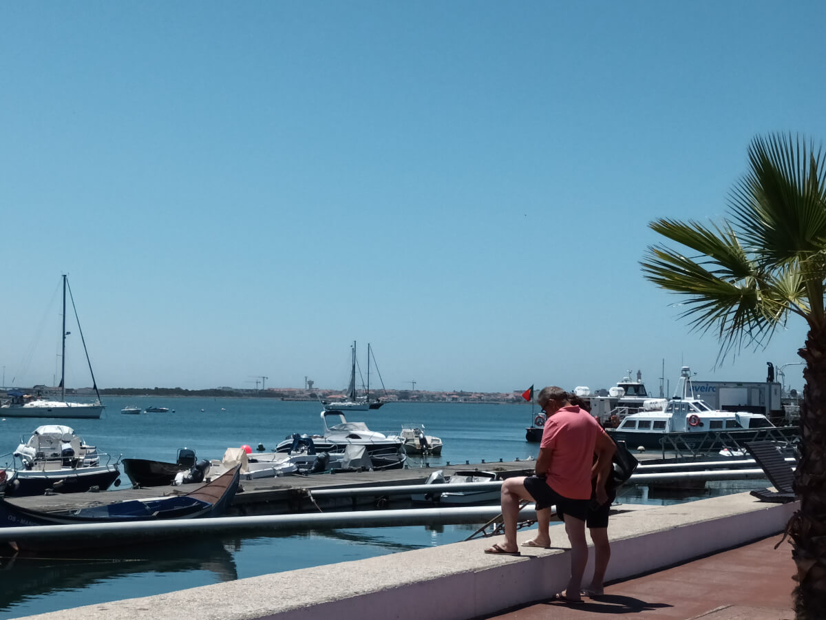 Image: The photo shows two tourist near the ferry pier in São Jacinto, Aveiro. In the background: the Praia de Barra beach community.