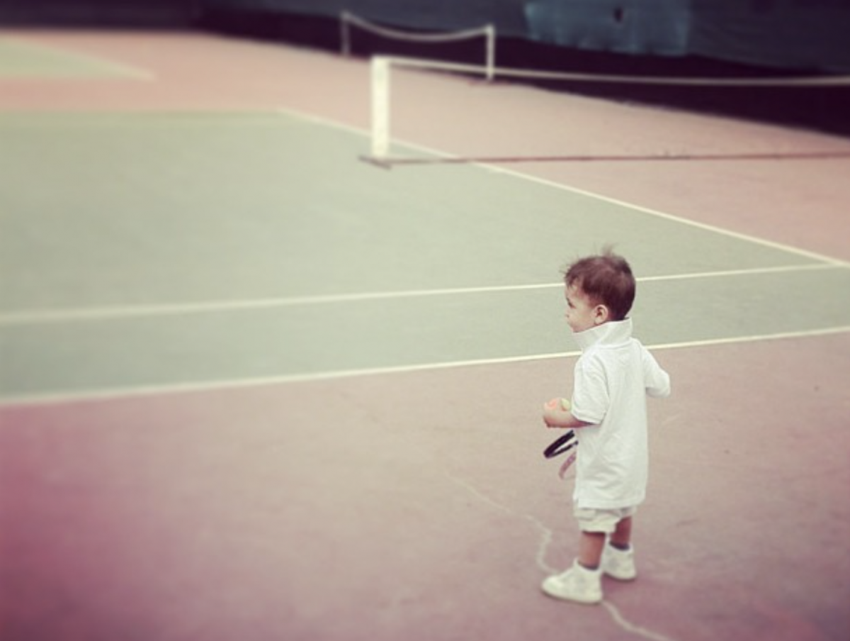 a boy dressed in all white with a tennis racquet and a ball on a tennis court