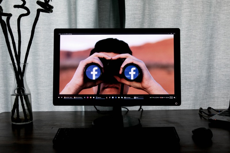 A computer desktop that has a person on binoculars that are owned by Facebook to signify Facebook's invasive privacy practices.